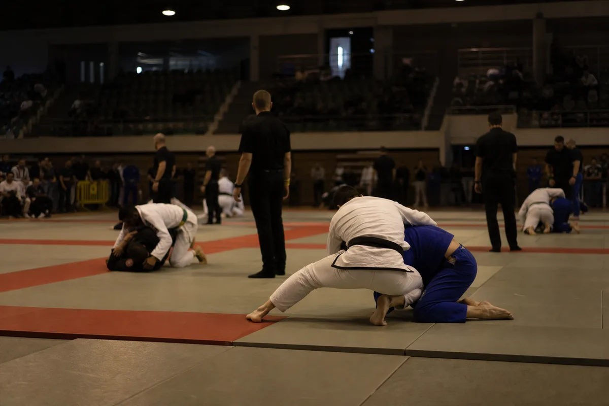 Salle de compétition de jiu-jitsu avec plusieurs tapis, arbitres et compétiteurs en kimono