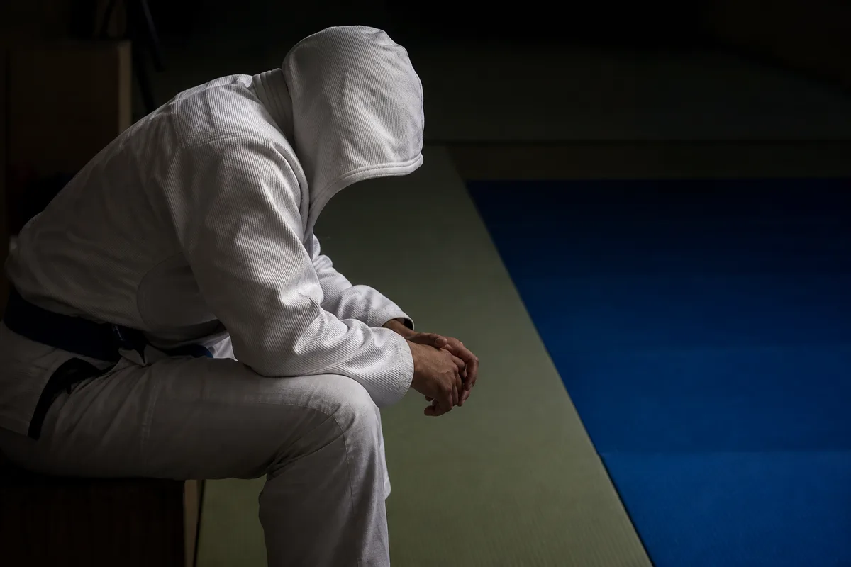 Compétiteur de jiu-jitsu assis au bord du tapis, capuche relevée, avant son combat