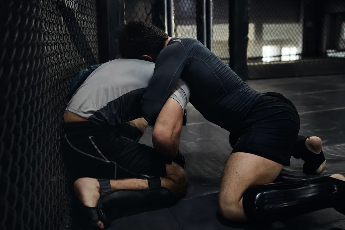 Combattant de MMA plaquant son adversaire contre la cage, contrôle par sous-crochet