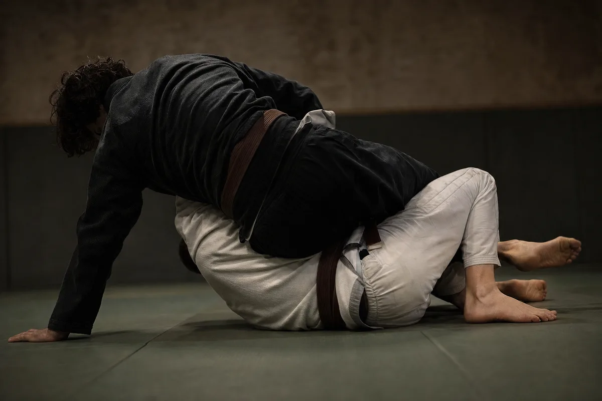 Pratiquant en kimono écrasant les hanches de son adversaire lors d&rsquo;un passage de garde