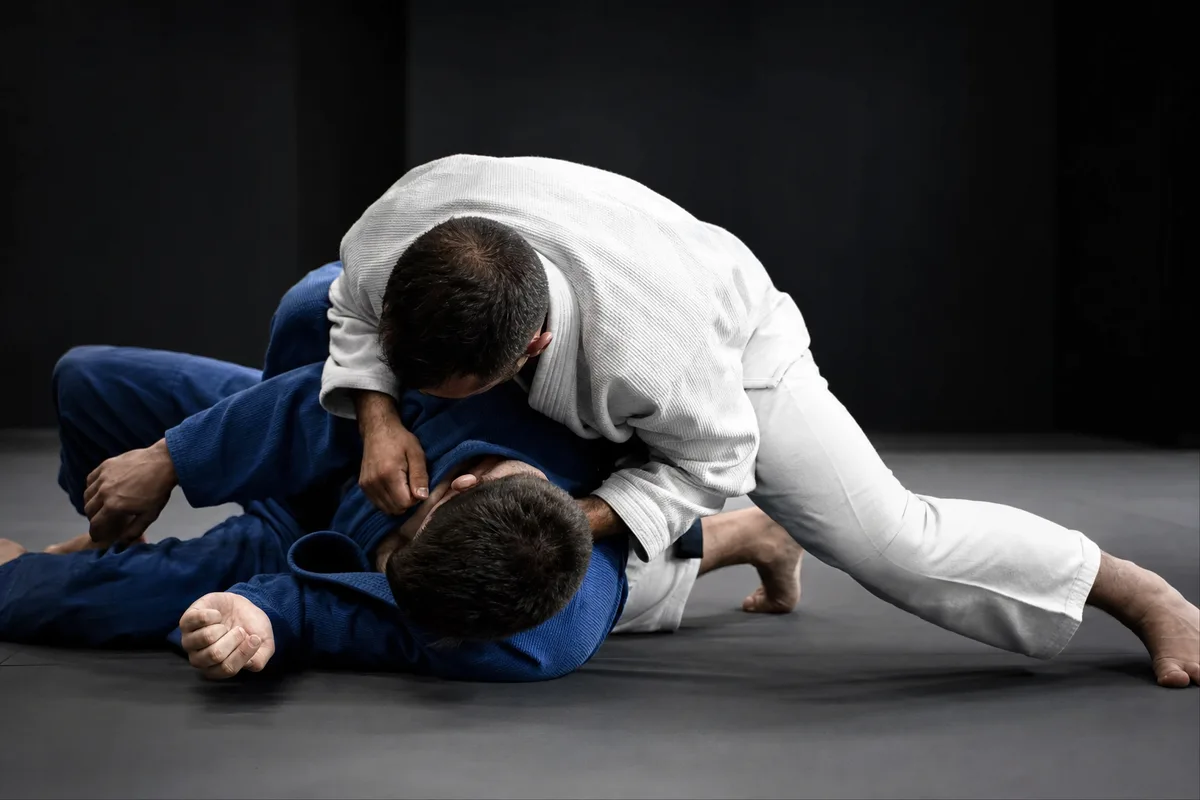 Deux pratiquants en kimono, l&rsquo;un maintenant un contrôle latéral au sol sur un tatami