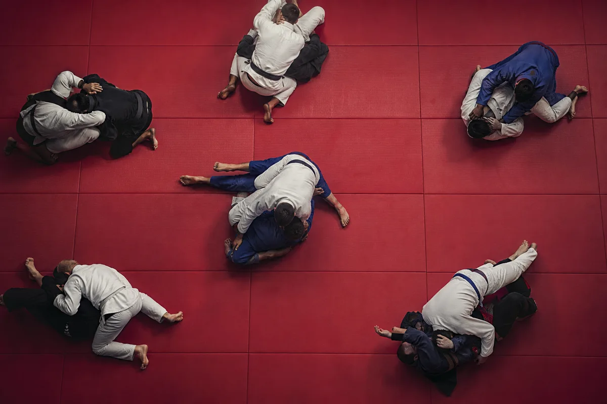 Salle de jiu-jitsu vue de haut avec plusieurs binômes en sparring sur un tapis rouge